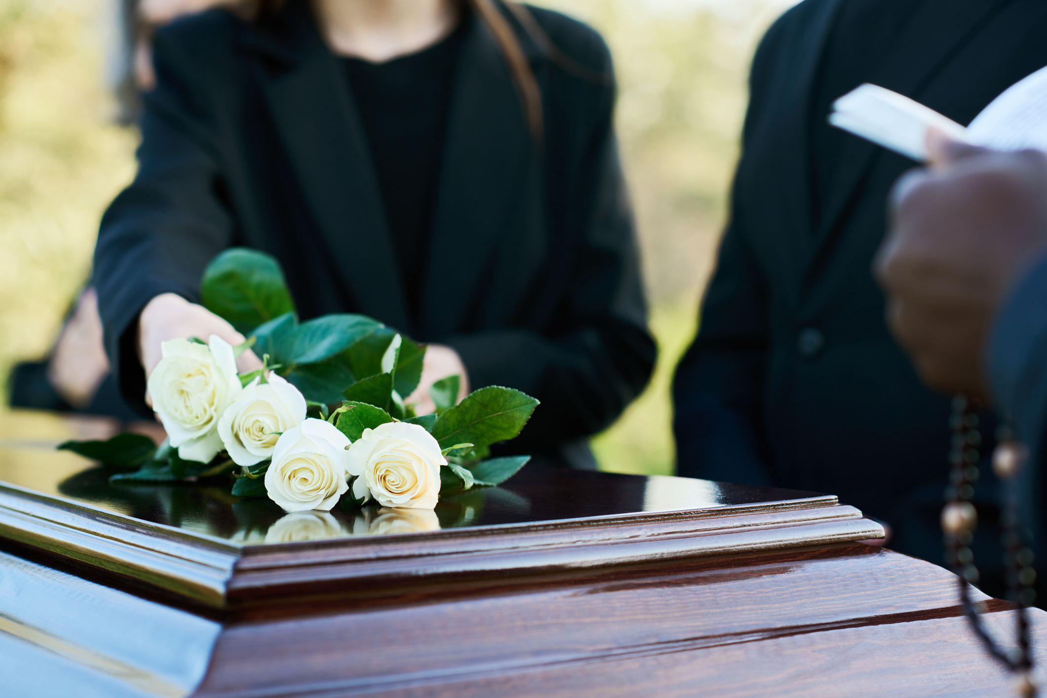 A grieving woman places white roses on the coffin of her deceased loved one.